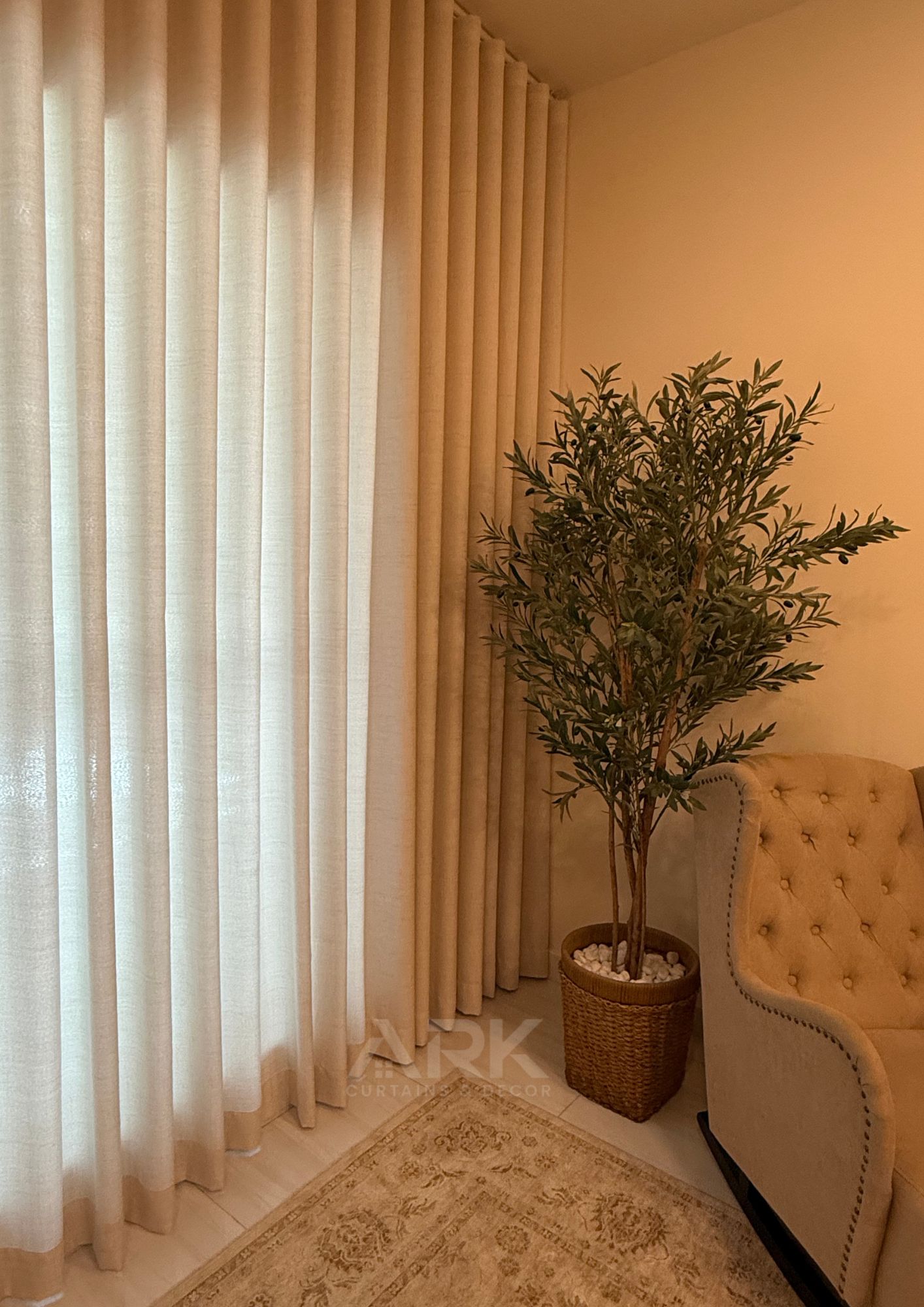 Cream sheer curtains beside an armchair and indoor plant